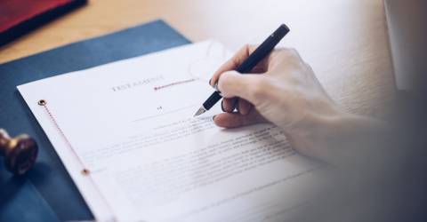 Een vrouw achter een bureau met een testament voor haar en een pen in haar hand